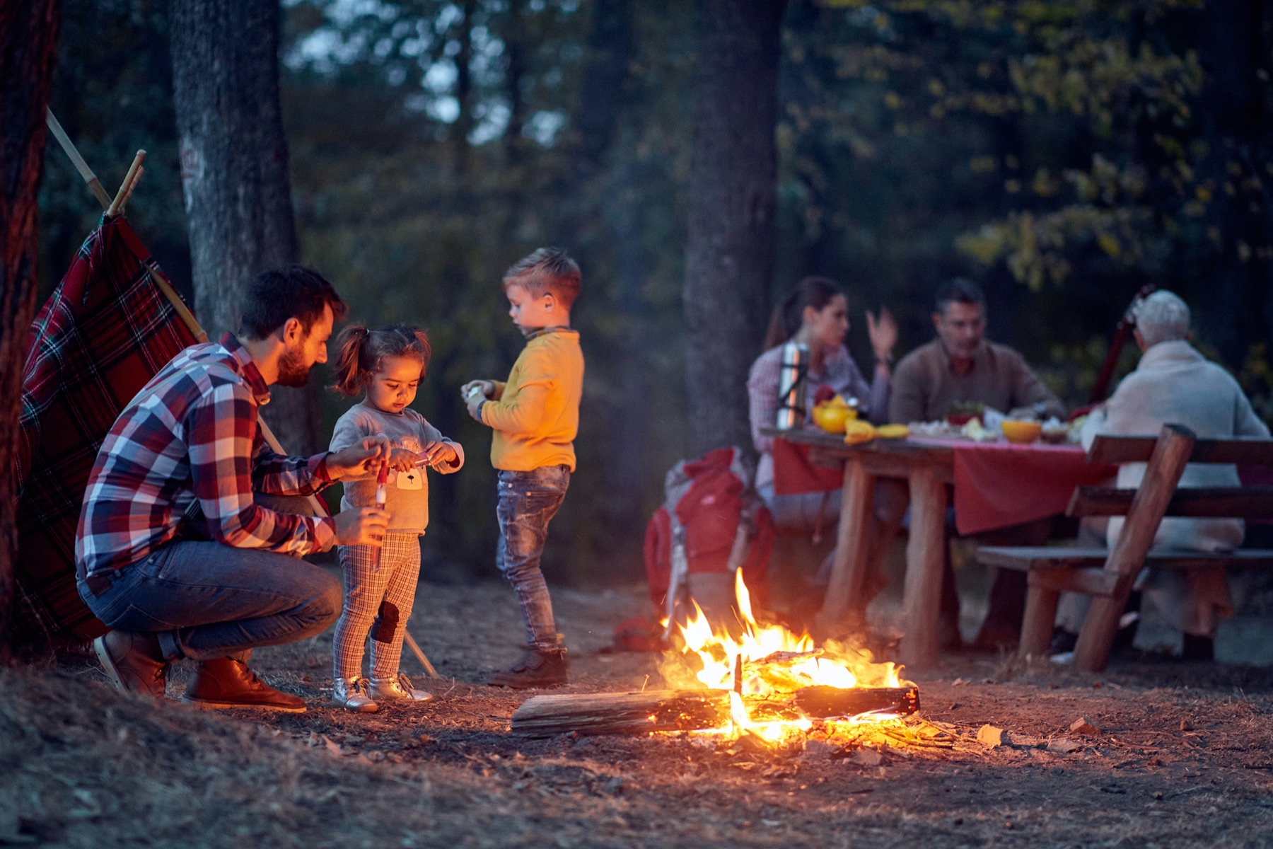 A family gathered around a campfire in the woods at dusk